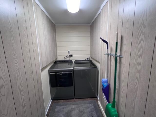 laundry room with laundry area, crown molding, wood walls, and washing machine and clothes dryer