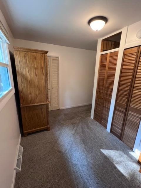 unfurnished bedroom with carpet, visible vents, two closets, and baseboards