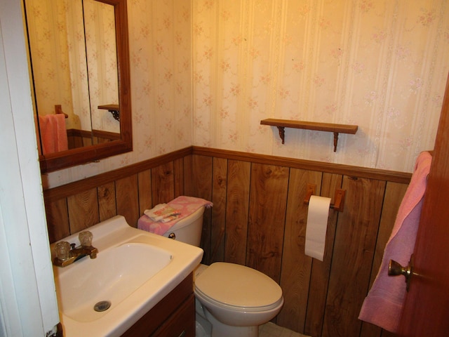 bathroom with vanity, a wainscoted wall, wallpapered walls, wood walls, and toilet