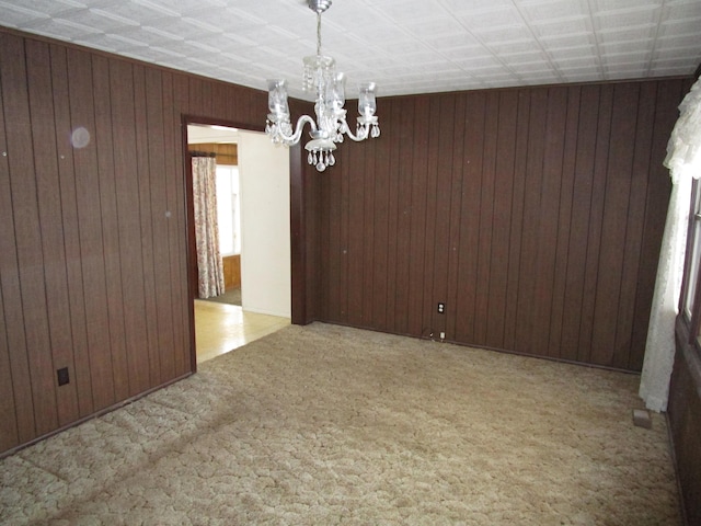 carpeted empty room featuring a notable chandelier and wood walls