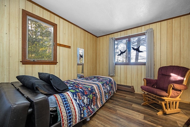 bedroom with a baseboard heating unit, wooden walls, wood finished floors, and ornamental molding