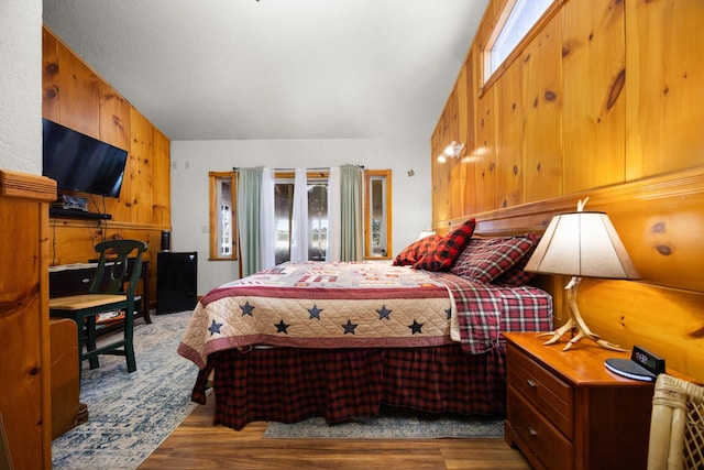 bedroom with multiple windows, wooden walls, wood finished floors, and vaulted ceiling