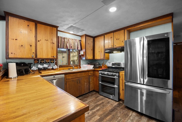 kitchen featuring brown cabinetry, under cabinet range hood, dark wood-style floors, stainless steel appliances, and a sink