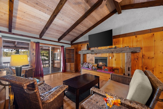 living area with wooden walls, beamed ceiling, wood ceiling, wood finished floors, and a glass covered fireplace