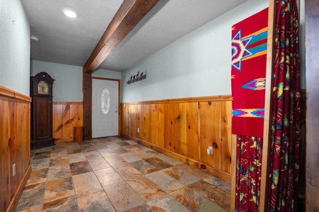 entrance foyer with a wainscoted wall, wooden walls, beamed ceiling, and stone finish flooring