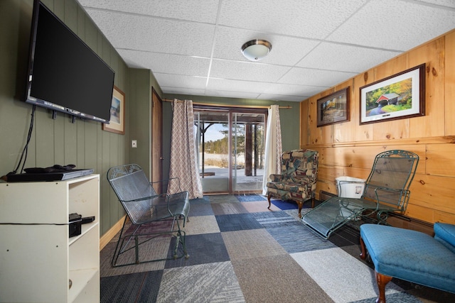 living area featuring a paneled ceiling, carpet, and wood walls