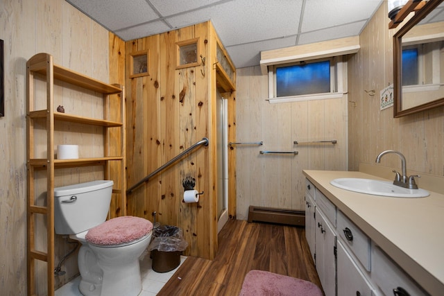 full bath with wood walls, toilet, baseboard heating, wood finished floors, and vanity