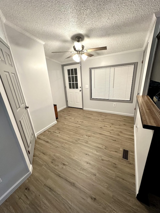 interior space with visible vents, crown molding, baseboards, wood finished floors, and a ceiling fan