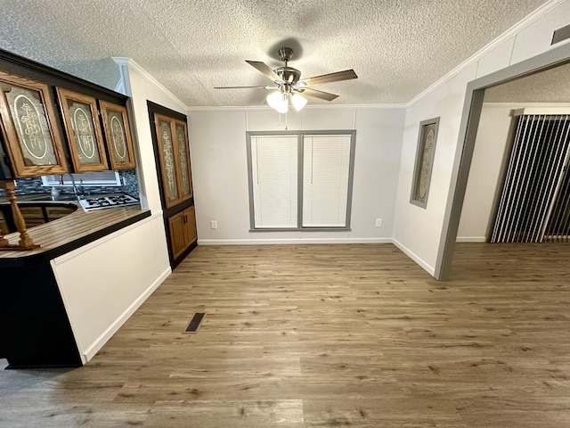 unfurnished dining area with a textured ceiling, a ceiling fan, wood finished floors, and ornamental molding