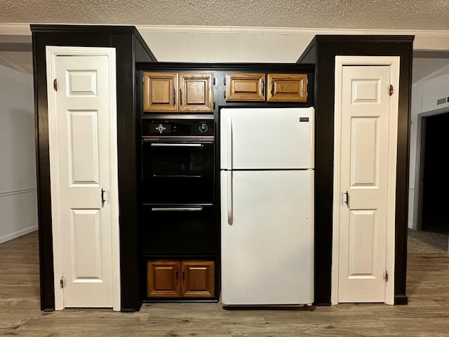 kitchen featuring crown molding, a textured ceiling, freestanding refrigerator, and light wood-style floors