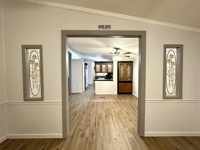 hallway featuring wood finished floors, visible vents, ornamental molding, vaulted ceiling, and a textured ceiling