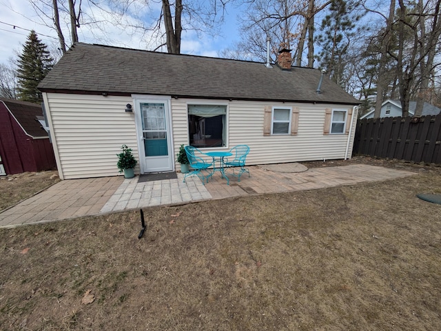 back of house featuring a lawn, a patio, roof with shingles, fence, and a chimney