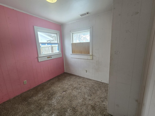 unfurnished room with visible vents, ornamental molding, wooden walls, and carpet flooring