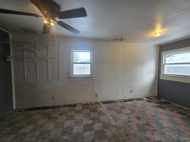 empty room with a wealth of natural light, wooden walls, a ceiling fan, and visible vents