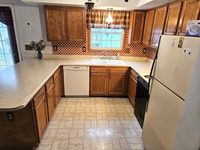 kitchen featuring brown cabinets, a sink, tasteful backsplash, white appliances, and a peninsula