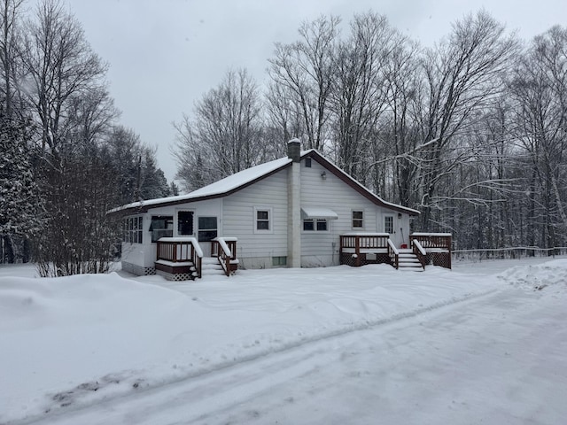 snow covered house featuring a chimney and a deck