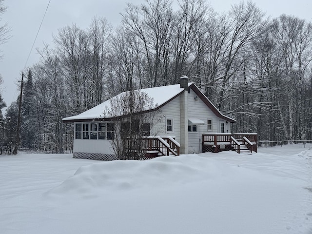 view of snowy exterior with a sunroom, a forest view, a wooden deck, and a chimney