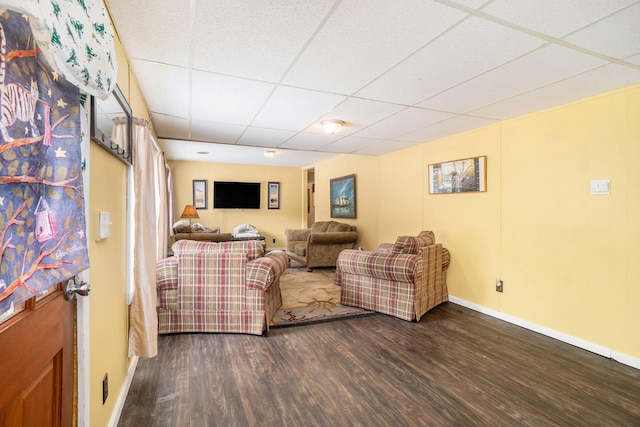 living room featuring a drop ceiling, baseboards, and wood finished floors