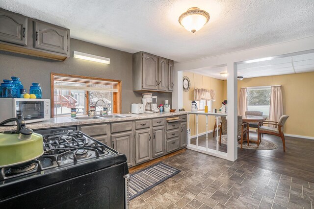 kitchen featuring white microwave, baseboards, a sink, light countertops, and black range with gas cooktop