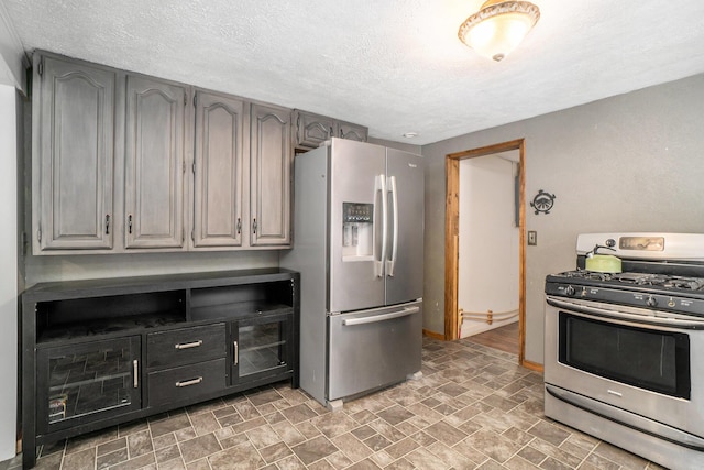 kitchen featuring a textured ceiling, stone finish floor, gray cabinetry, and stainless steel appliances