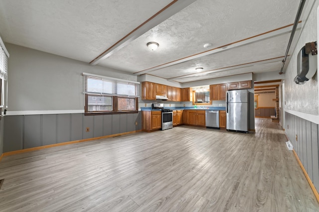 kitchen with light wood finished floors, under cabinet range hood, appliances with stainless steel finishes, brown cabinetry, and a textured ceiling