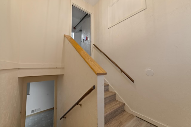 staircase with wood finished floors, visible vents, and baseboards