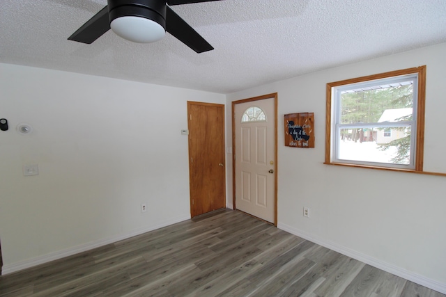 interior space featuring a textured ceiling, a ceiling fan, baseboards, and wood finished floors