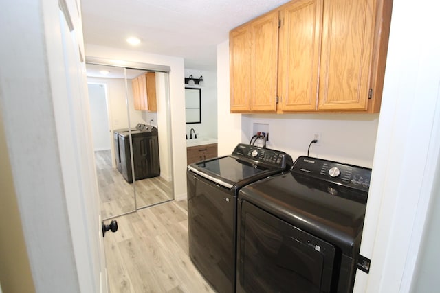 washroom featuring washing machine and clothes dryer, light wood-type flooring, recessed lighting, cabinet space, and a sink