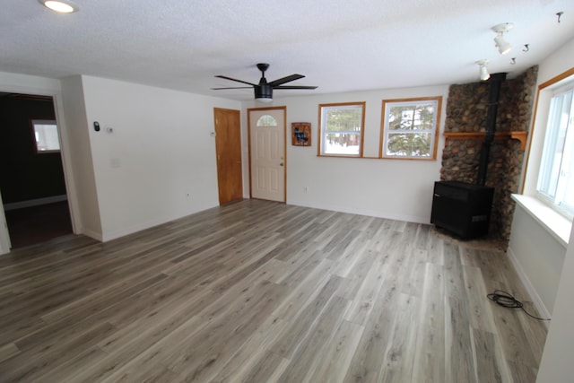 unfurnished living room featuring wood finished floors, a wood stove, a healthy amount of sunlight, and baseboards