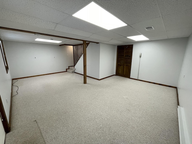 finished basement featuring stairway, baseboards, visible vents, a paneled ceiling, and light carpet