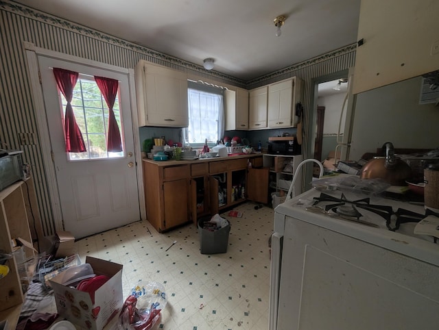 kitchen featuring black microwave, light floors, white gas range oven, and white cabinetry