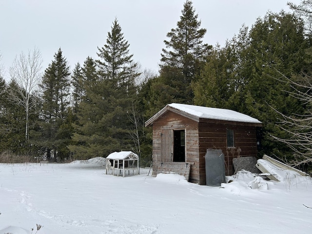 snow covered structure featuring an outbuilding and a wooded view