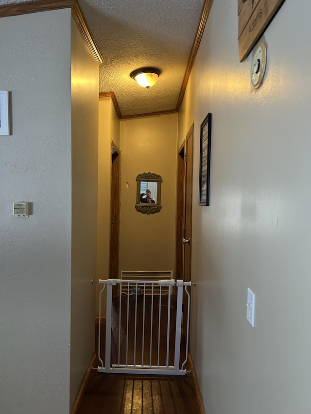 hall with wood finished floors, a textured ceiling, and ornamental molding