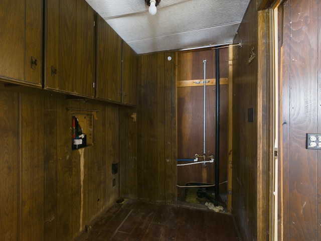 clothes washing area featuring dark wood-style floors, wooden walls, and a textured ceiling