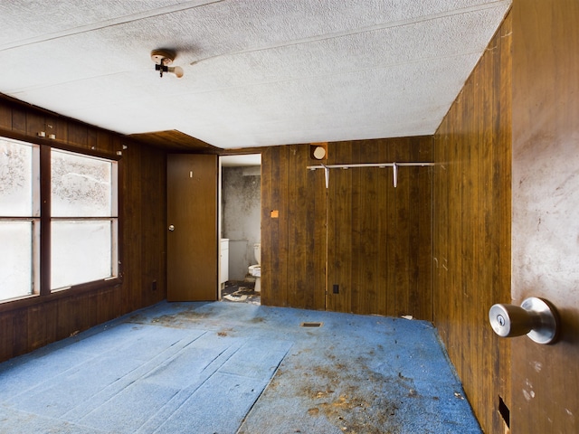 carpeted spare room with wooden walls and a textured ceiling