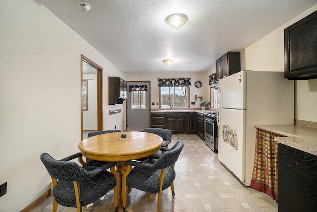kitchen with a sink, a textured ceiling, freestanding refrigerator, light countertops, and stainless steel gas range