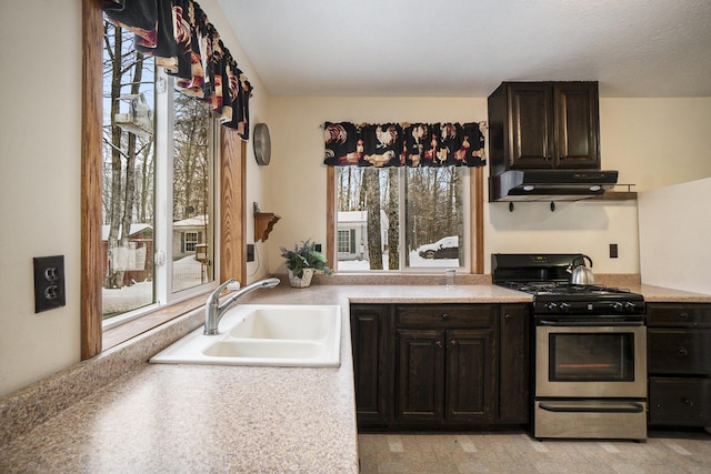 kitchen featuring a sink, range hood, dark brown cabinetry, light countertops, and stainless steel gas range