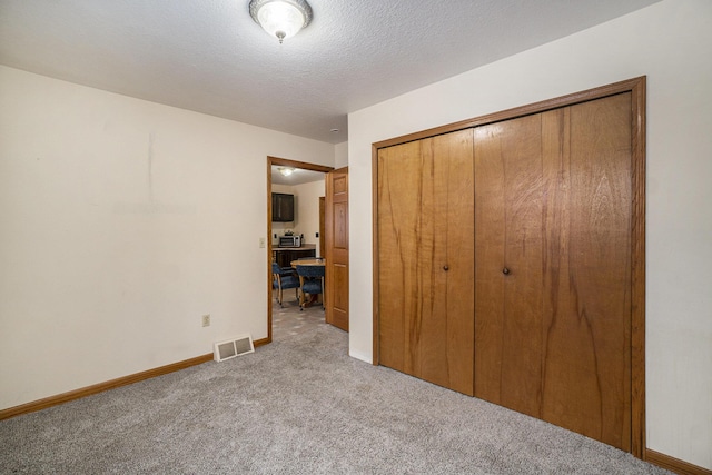 unfurnished bedroom featuring visible vents, light carpet, a textured ceiling, a closet, and baseboards