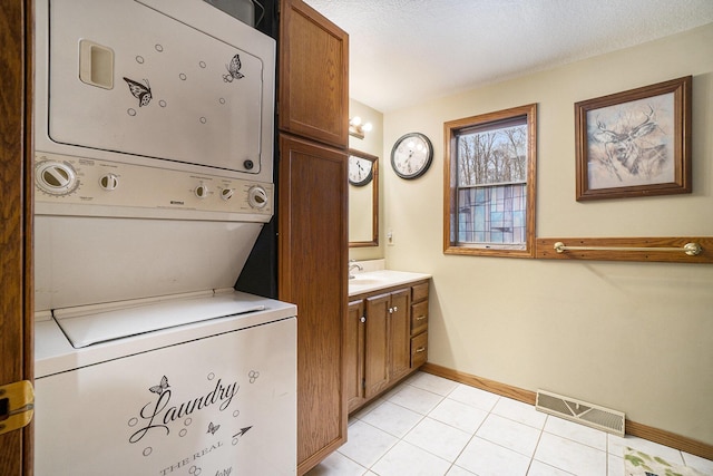 laundry area featuring visible vents, baseboards, light tile patterned floors, stacked washing maching and dryer, and cabinet space