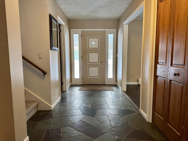 foyer featuring stone tile flooring, stairway, a textured ceiling, and baseboards