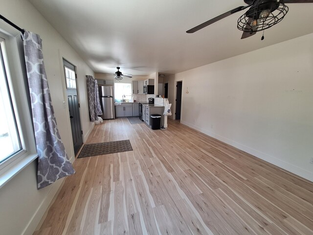 unfurnished living room with a ceiling fan, baseboards, light wood-style floors, and a sink