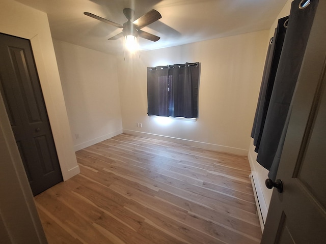 unfurnished bedroom with light wood finished floors, baseboard heating, baseboards, and a ceiling fan