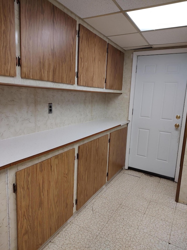 kitchen with brown cabinetry, light floors, light countertops, and a paneled ceiling