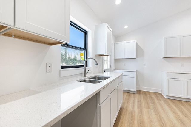 kitchen with light stone counters, recessed lighting, light wood-style flooring, white cabinets, and a sink