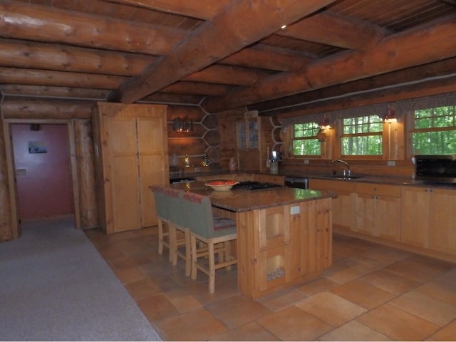 kitchen with a breakfast bar, beam ceiling, a sink, light brown cabinetry, and rustic walls