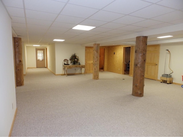 finished basement with wooden walls, carpet flooring, a paneled ceiling, and baseboards