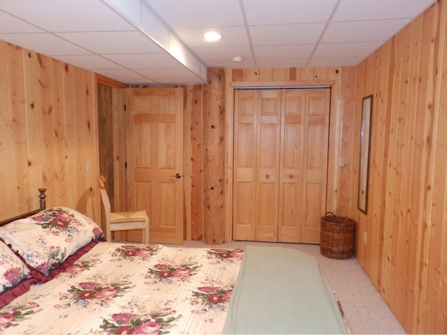 carpeted bedroom featuring a closet, a paneled ceiling, and wood walls