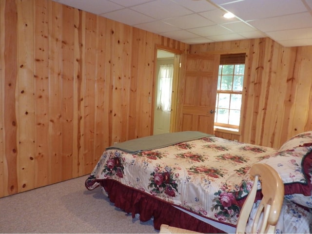 bedroom with a drop ceiling, wood walls, and carpet