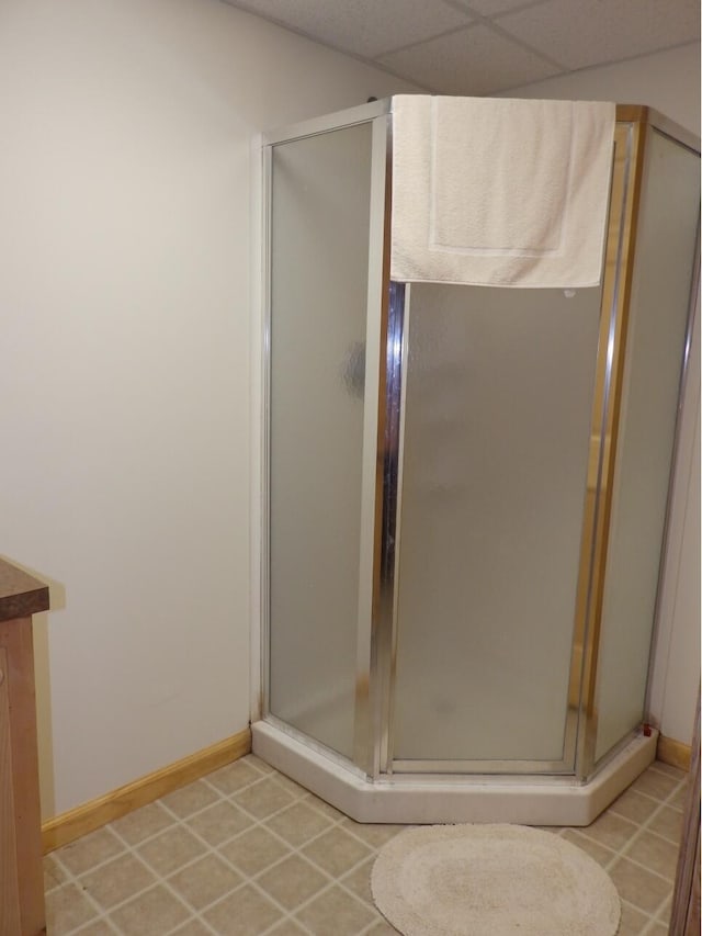 full bathroom with tile patterned flooring, a shower stall, a paneled ceiling, and baseboards