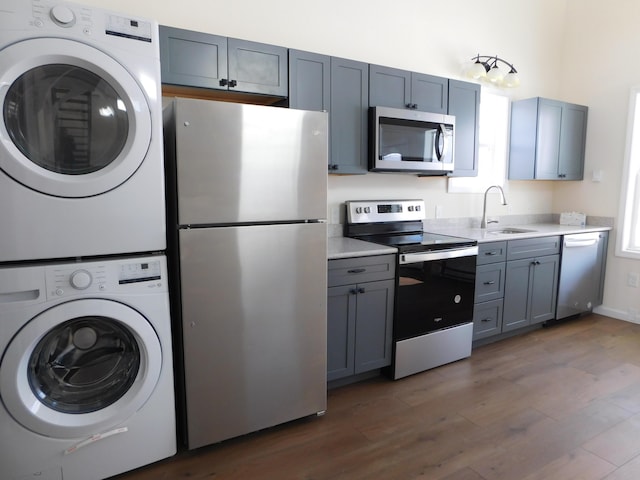 kitchen featuring dark wood-style floors, a sink, light countertops, appliances with stainless steel finishes, and stacked washer / dryer